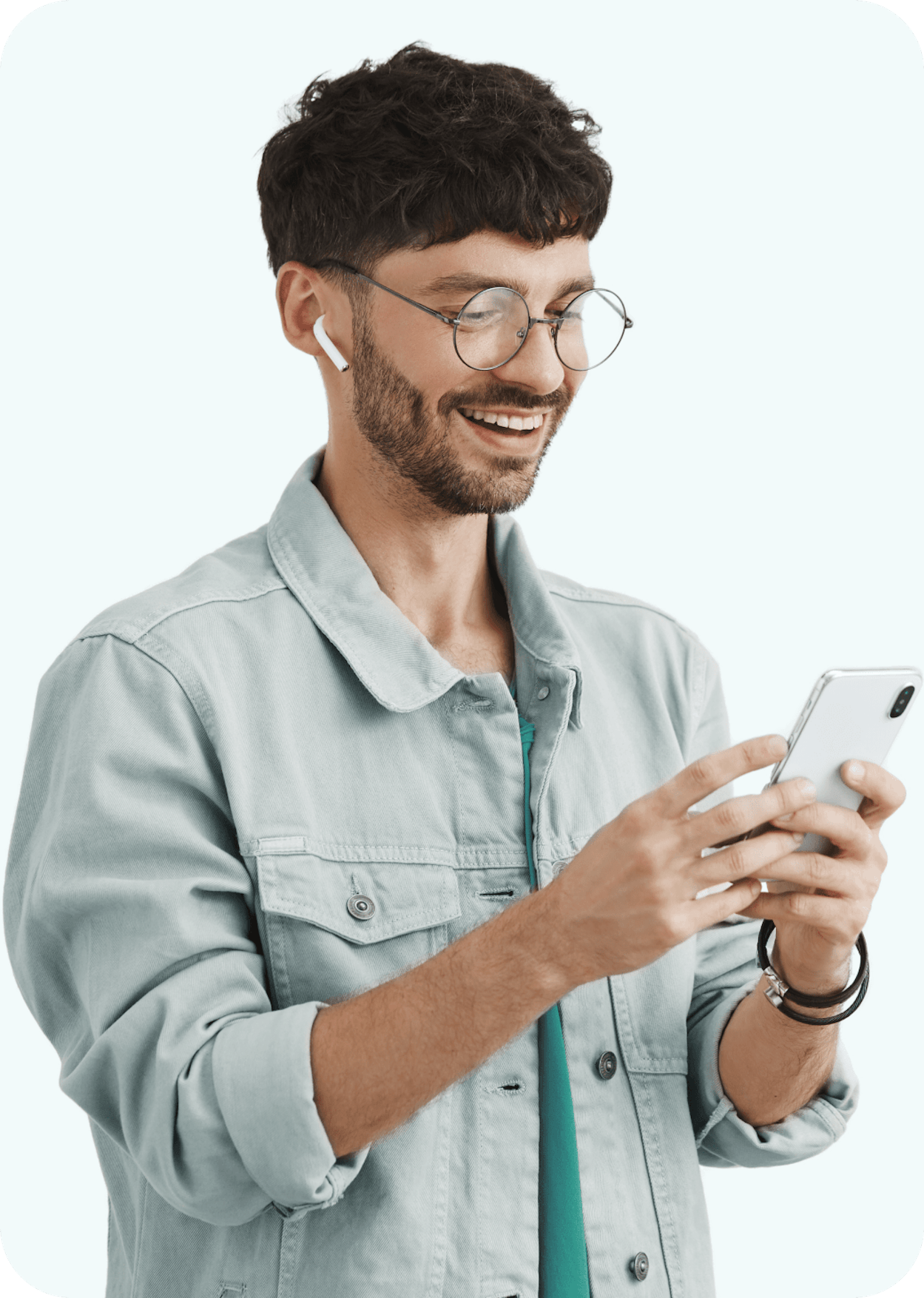 Person smiling while using smartphone, wearing wireless earbuds, round glasses and light denim jacket against white background